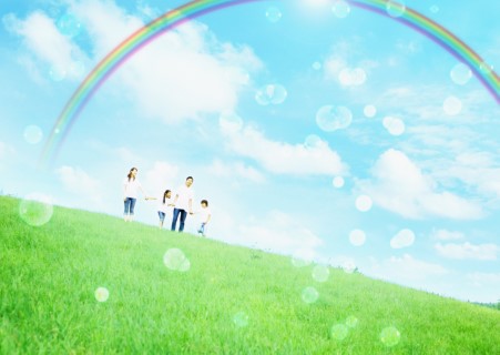 Family walking on a green hill with a rainbow and bubbles flying