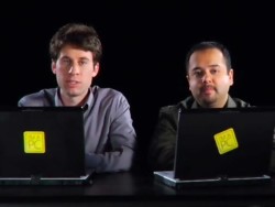 Two people in front of laptops looking towards the camera